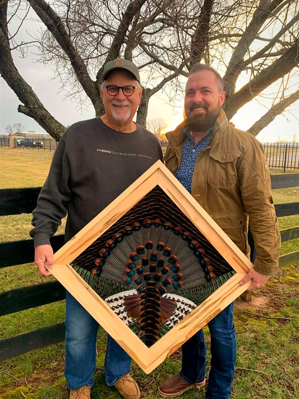 Mark Cooke delivering a finished ocellated turkey fan in a maple diamond frame to a smiling client at sunset