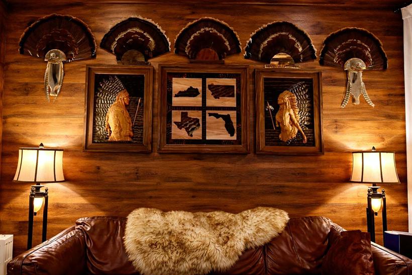 A client's collector wall — five turkey fan mounts above the Native American series and a four-state frame, lit warmly by twin lamps